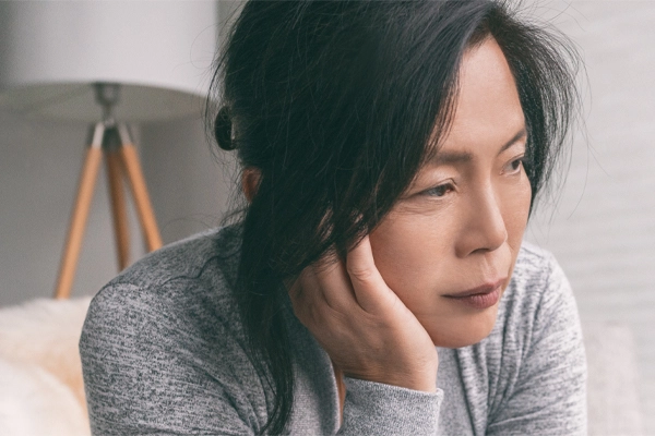 Adrenal-Fatigue-Doctor A middle-aged asian woman sitting on her couch, resting her head on her hand, suffering from adrenal fatigue. Get treatment for adrenal fatigue syndrome from David Garcia, D.O. in Nashville Metro.
