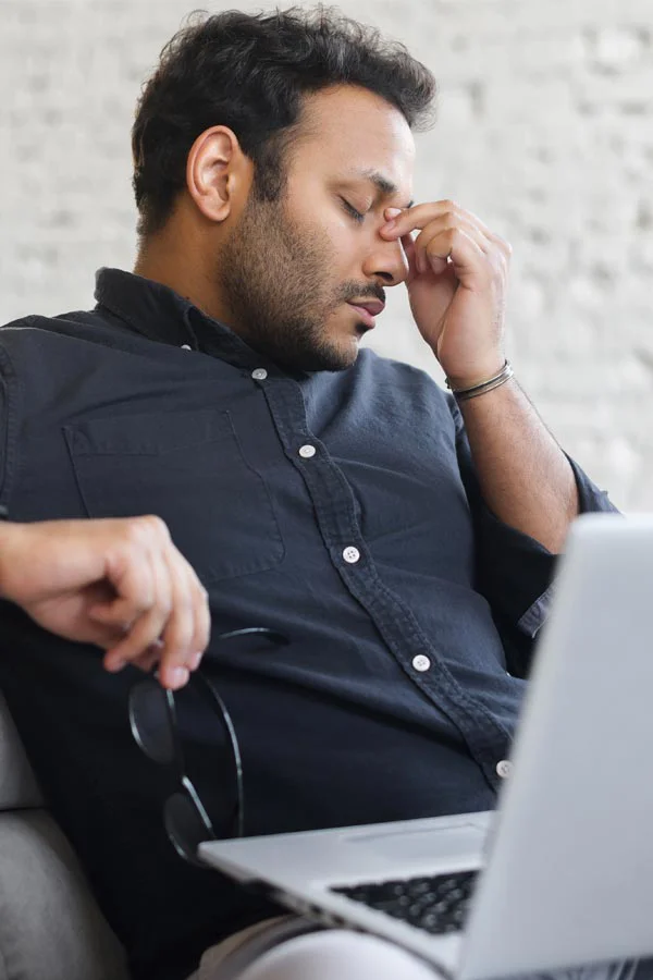 Adrenal-Fatigue-Treatment A middle-aged man with a laptop closing his eyes and rubbing his nose. He needs treatment for Adrenal Fatigue Syndrome from David Garcia, D.O. in Nashville Metro.