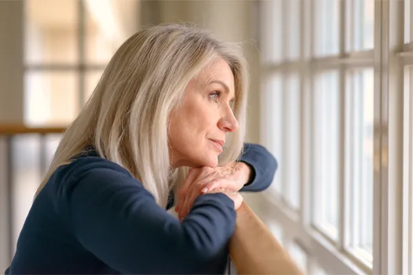 Adrenal-Hormone-Disorder-Clinic A mature woman in a blue shirt looks out the window with melancholy. Schedule treatment for adrenal hormone disorder from David Garcia, D.O. in Nashville Metro.