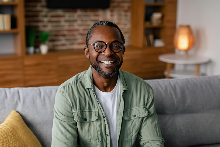 Andropause-Doctor A middle aged black man in a green button up shirt sits on his couch smiling, happy with his treatment for andropause and low testosterone from David Garcia, D.O. in Nashville Metro.