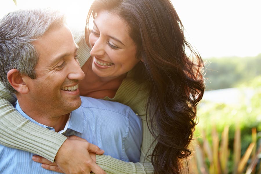 Bioidentical-Hormone-Pellet-Therapy-Clinic Smiling middle-aged couple embracing outdoors in a sunlit natural setting. Schedule your bioidentical hormone pellet therapy consultation with David Garcia, D.O. in Nashville Metro.