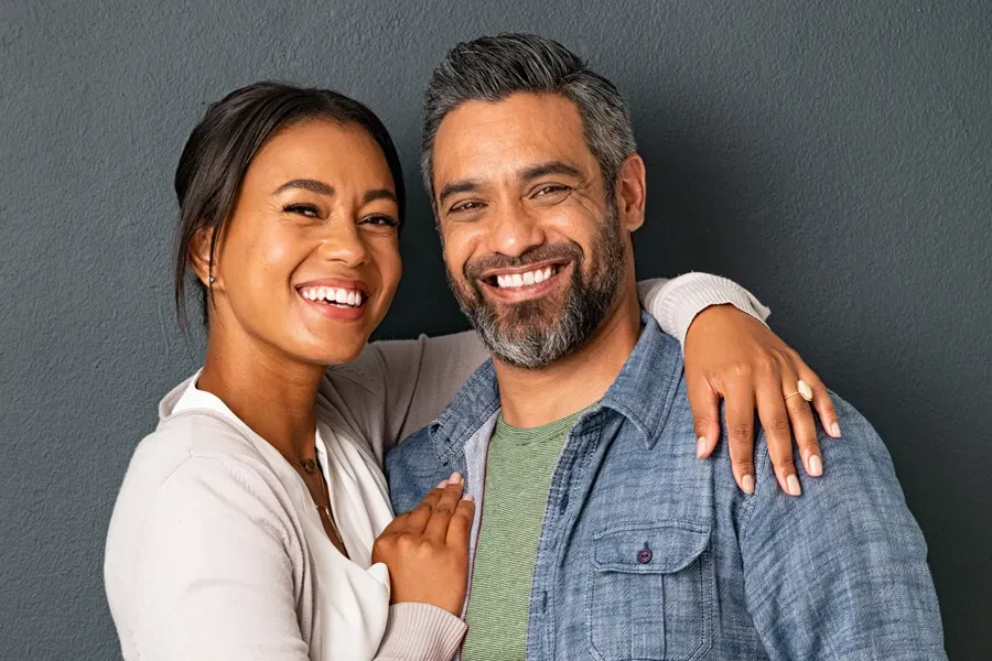 Bioidentical-Hormone-Therapy-Doctor A middle-aged couple with their arms around each other standing against a gray background and smiling, happy with the bioidentical hormone therapy they received from David Garcia, D.O. in Nashville Metro.