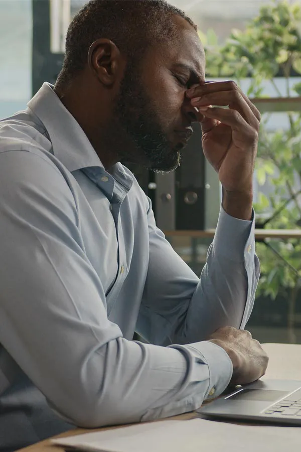 Chronic-Fatigue-Treatment A black man rubbing the top of his nose at his desk, in need of chronic fatigue treatment from David Garcia, D.O. in Nashville Metro.