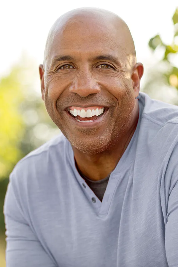 Healthy-Aging-Peptides-Treatment A middle-aged black man in a gray v-neck t-shirt sits outside smiling, happy with the healthy aging peptide treatments from David Garcia, D.O. in Nashville Metro