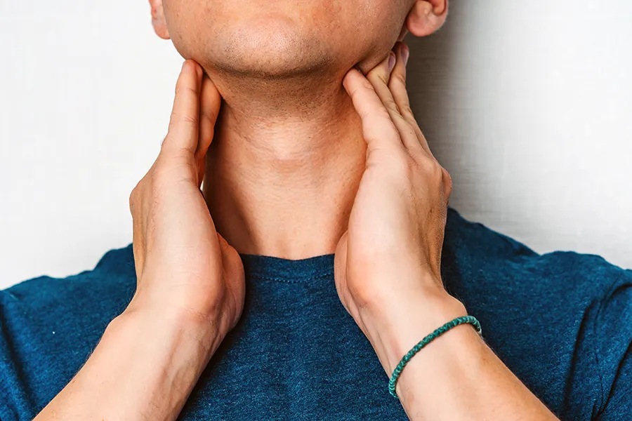 Hypothyroidism-Clinic A man in a dark teal shirt rubs the lymph nodes on his neck. Get hypothyroidism treatment from David Garcia, D.O. in Nashville Metro.