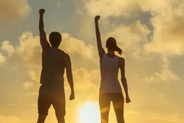 Ipamorelin-Peptide-Clinic A couple raise their right arms in the air in triumph, framed by the sunrise. Get Ipamorelin peptide treatment from David Garcia, D.O. in Nashville Metro.