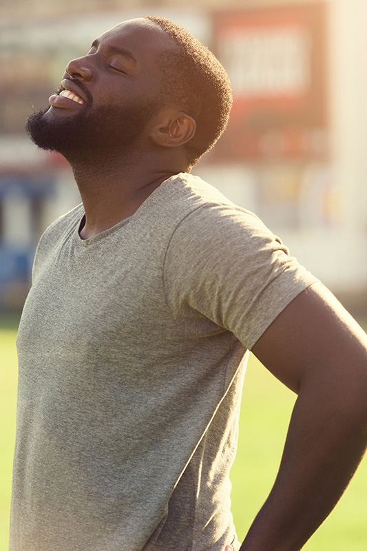 Lean-Muscle-and-Recovery-Treatment A black man in a gray t-shirt and smiles, looking up with closed eyes after a satisfying workout. Get treatment for lean muscle loss and recovery from David Garcia, D.O. in Nashville Metro.
