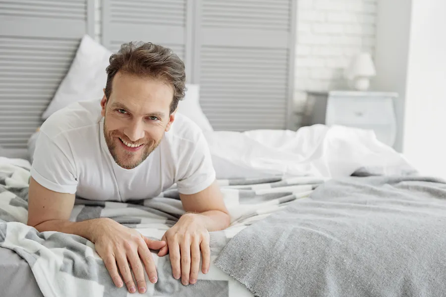 Low-Libido-in-Men-Doctor A dirty-blonde haired man lays on his stomach in bed smiling. Schedule treatment for low libido in men from David Garcia, D.O. in Nashville Metro.