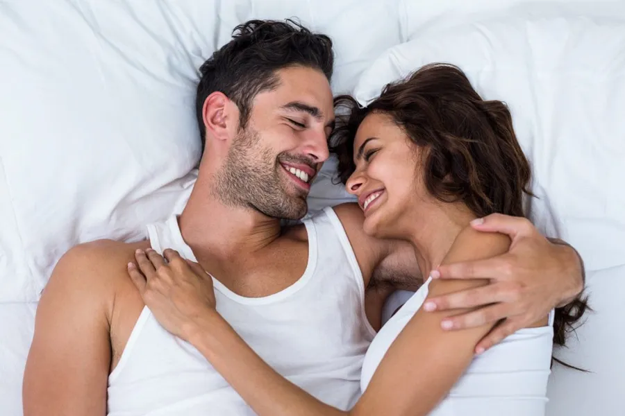 PT141-for-Men-Doctor A laughing man and woman in undershirts lie in each other's arms on a white bed, representing successful PT141 sexual wellness therapy for men from David Garcia, D.O. in Nashville Metro.
