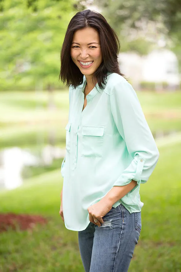 Perimenopause-Treatment A middle-aged brunette woman in a light green button-up shirt stands outside smiling, happy with her perimenopause treatment from David Garcia, D.O. in Nashville Metro.