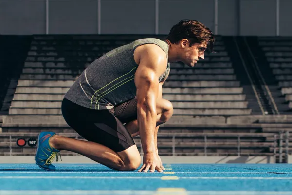 Sermorelin-Clinic With a determined look, Aamuscular man in track clothes kneels at the start of a race. Get Sermorelin peptide therapy from David Garcia, D.O. in Nashville Metro.