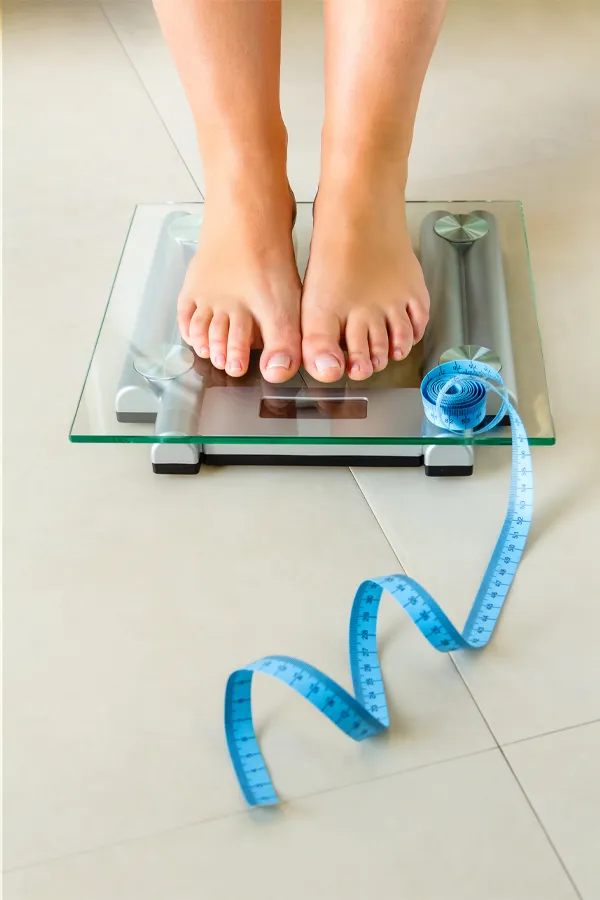Weight-Loss-Resistance-Treatment Close-up of a woman's feet standing on a scale, with measuring tape by her toes, getting treatment for weight loss resistance from David Garcia, D.O. in Nashville Metro.